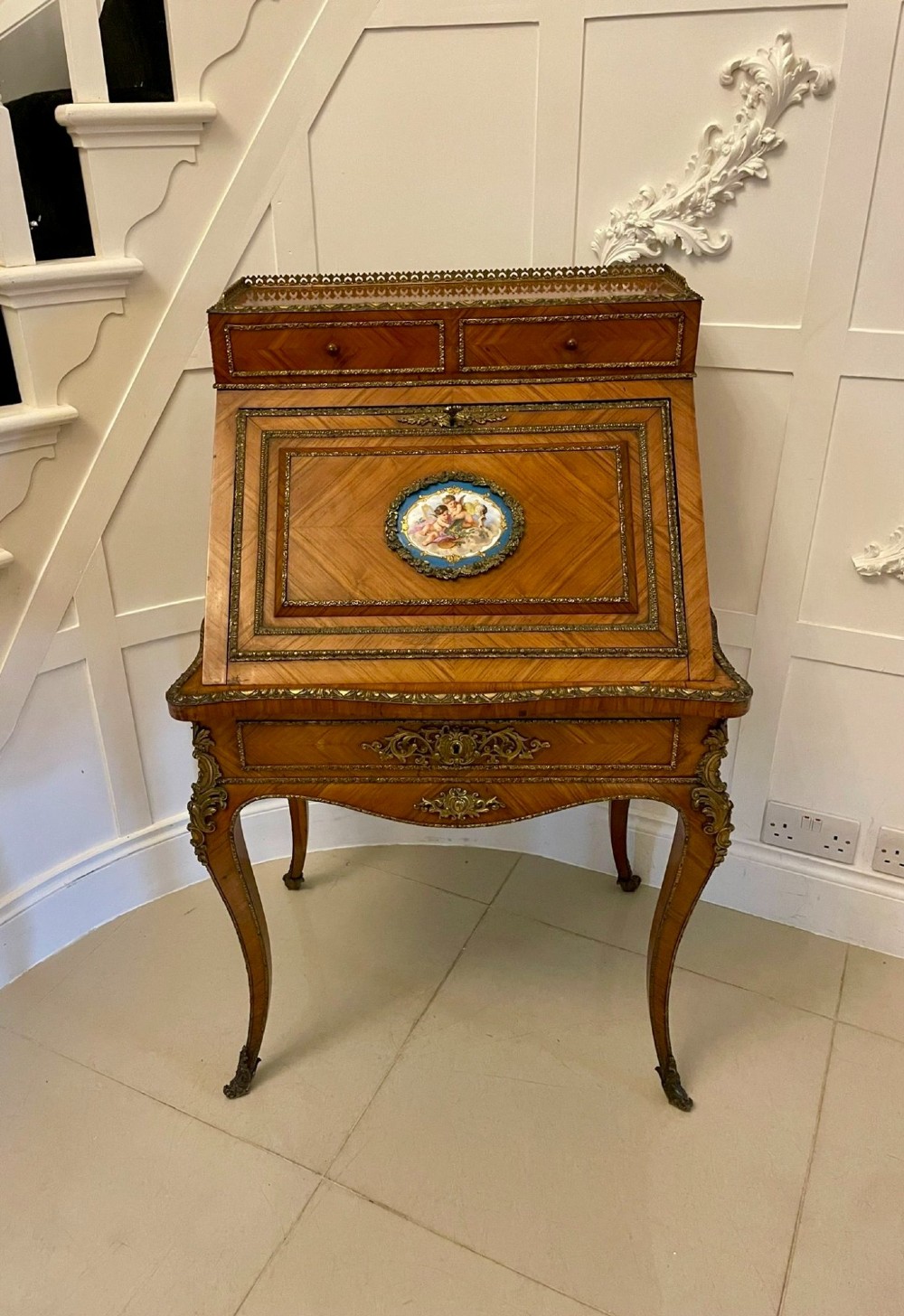 A French Rococo revival slant-front kingwood bureau featuring delicate ormolu mounts, a central hand-painted porcelain plaque, and elegant cabriole legs. View XV