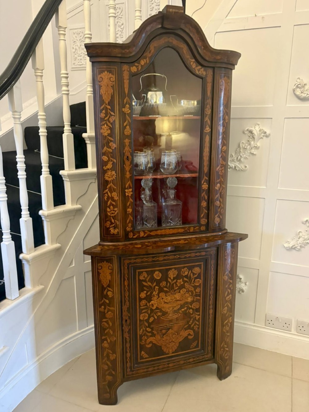 A 19th-century two-tier Dutch marquetry corner cabinet featuring intricate floral inlays, an arched glazed top door, and a solid lower cupboard door. View IV