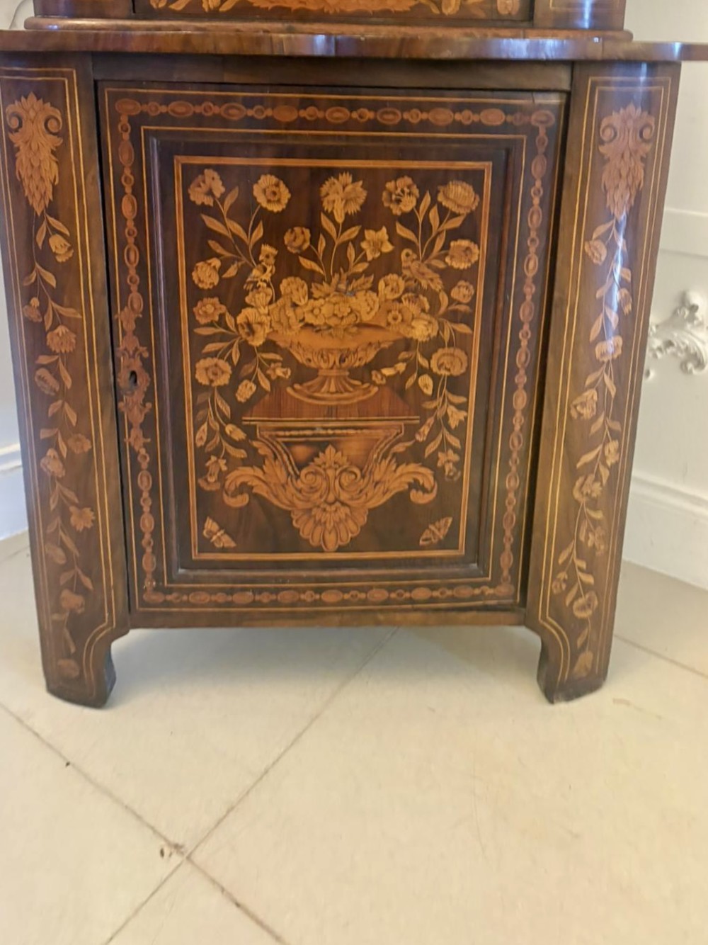 A 19th-century two-tier Dutch marquetry corner cabinet featuring intricate floral inlays, an arched glazed top door, and a solid lower cupboard door. View V