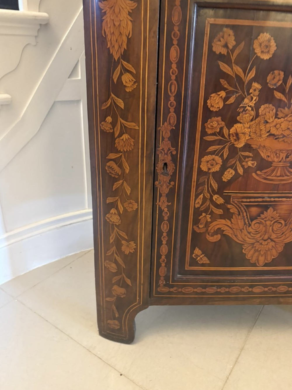 A 19th-century two-tier Dutch marquetry corner cabinet featuring intricate floral inlays, an arched glazed top door, and a solid lower cupboard door. View VII