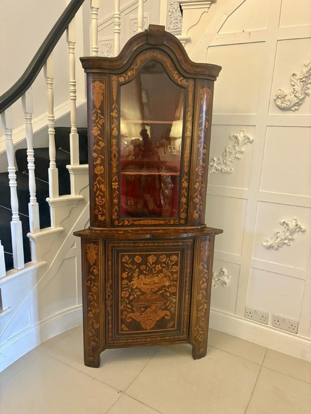 A 19th-century two-tier Dutch marquetry corner cabinet featuring intricate floral inlays, an arched glazed top door, and a solid lower cupboard door.