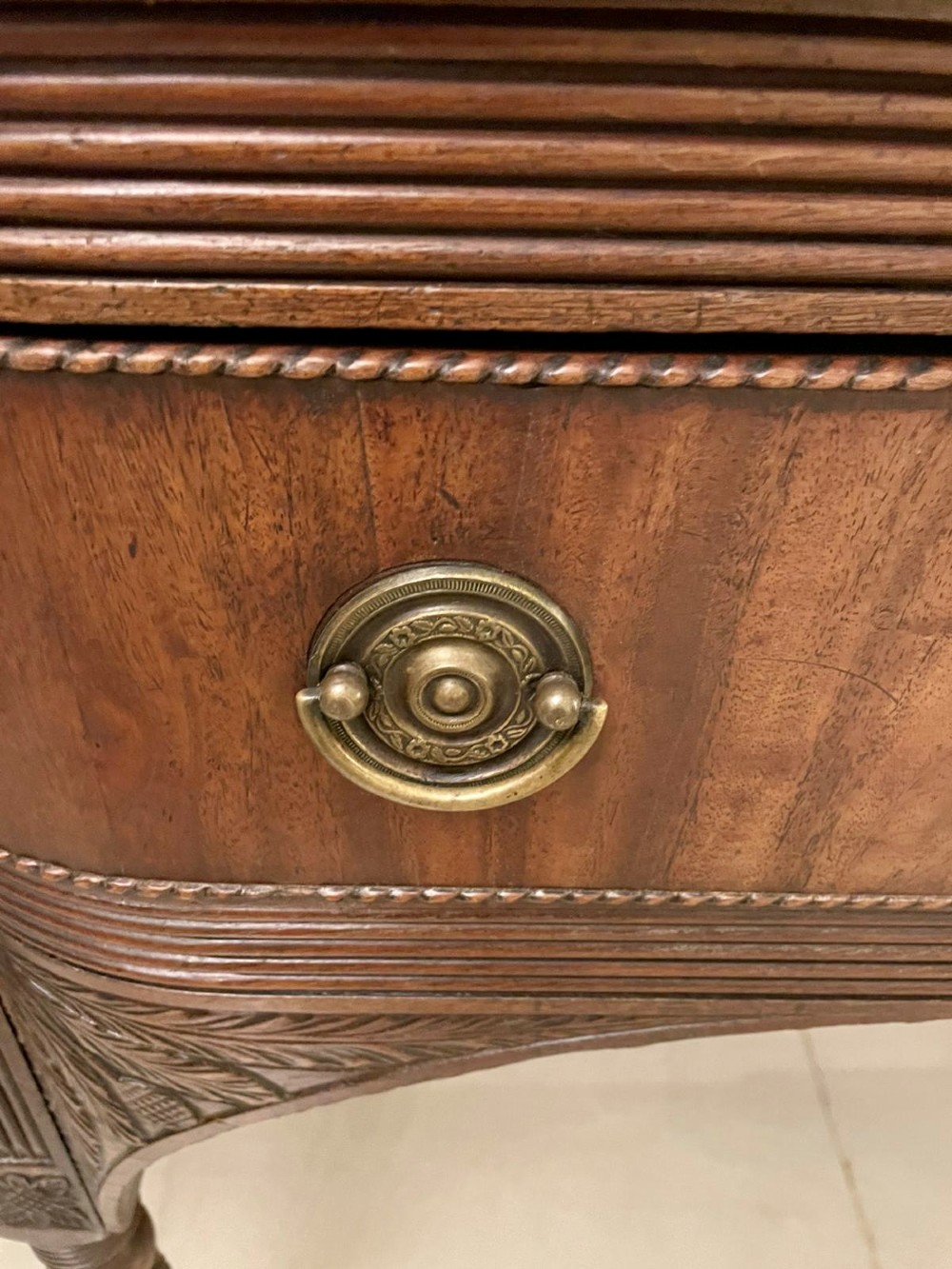 An antique George III mahogany breakfront sideboard featuring flame mahogany drawer fronts, reeded legs, and central drawer flanked by cupboards. View III