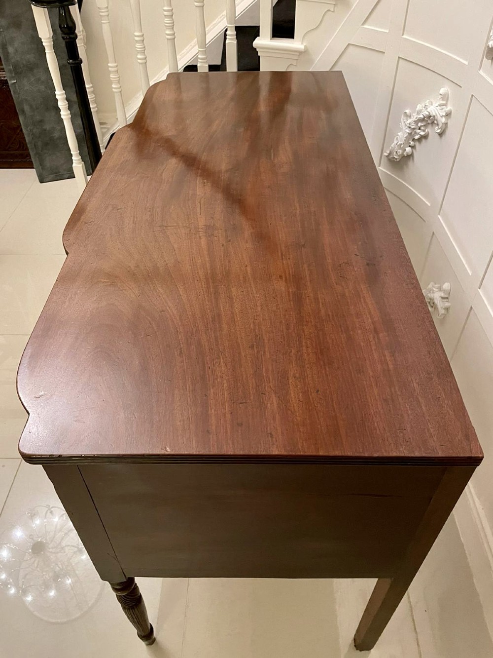 An antique George III mahogany breakfront sideboard featuring flame mahogany drawer fronts, reeded legs, and central drawer flanked by cupboards. View IV