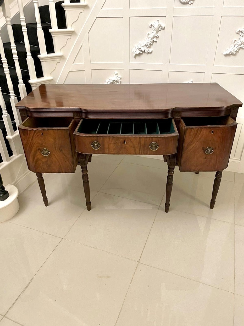 An antique George III mahogany breakfront sideboard featuring flame mahogany drawer fronts, reeded legs, and central drawer flanked by cupboards. View V