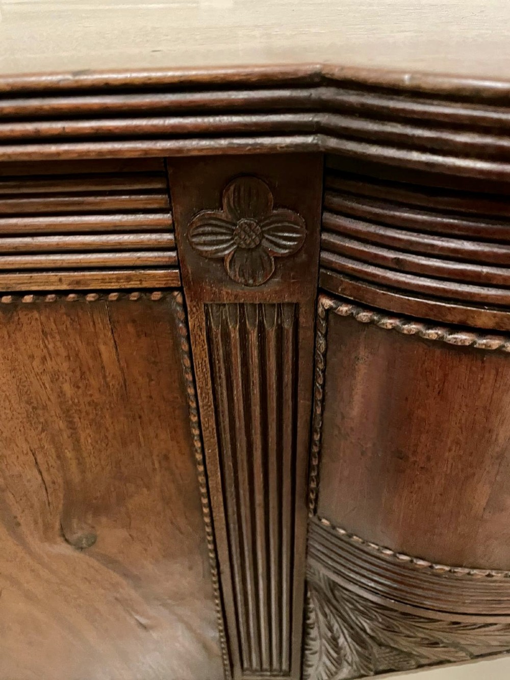An antique George III mahogany breakfront sideboard featuring flame mahogany drawer fronts, reeded legs, and central drawer flanked by cupboards. View VI