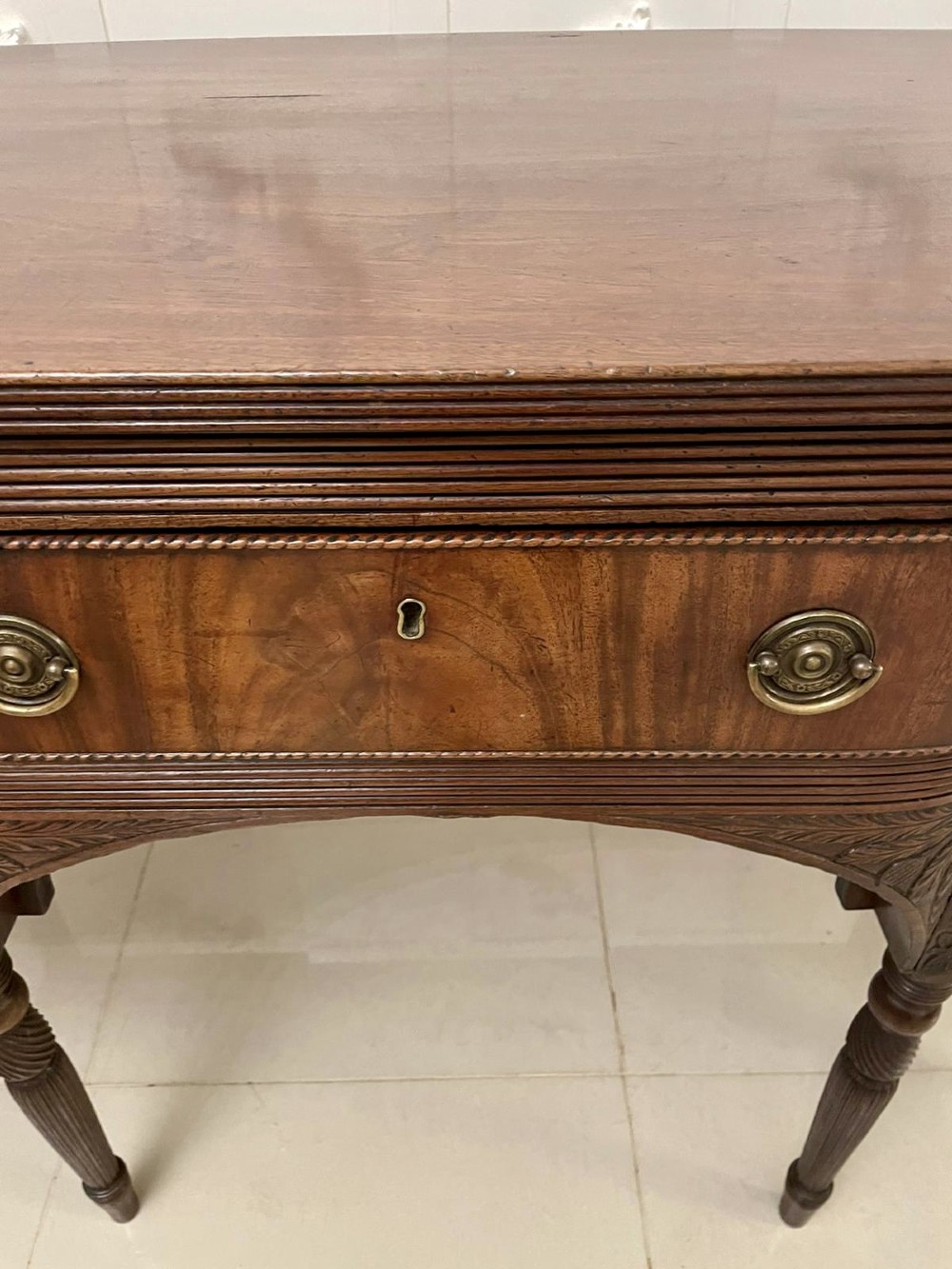 An antique George III mahogany breakfront sideboard featuring flame mahogany drawer fronts, reeded legs, and central drawer flanked by cupboards. View VII