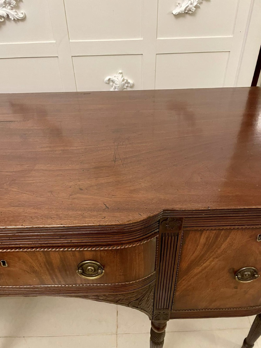 An antique George III mahogany breakfront sideboard featuring flame mahogany drawer fronts, reeded legs, and central drawer flanked by cupboards. View X