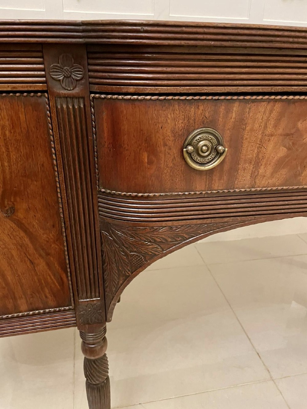 An antique George III mahogany breakfront sideboard featuring flame mahogany drawer fronts, reeded legs, and central drawer flanked by cupboards. View XIV