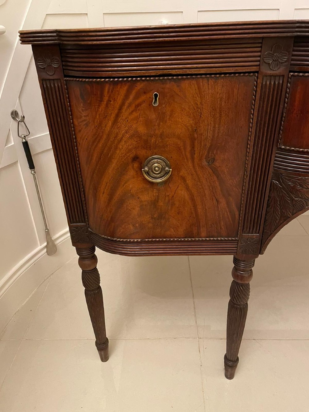 An antique George III mahogany breakfront sideboard featuring flame mahogany drawer fronts, reeded legs, and central drawer flanked by cupboards. View XV