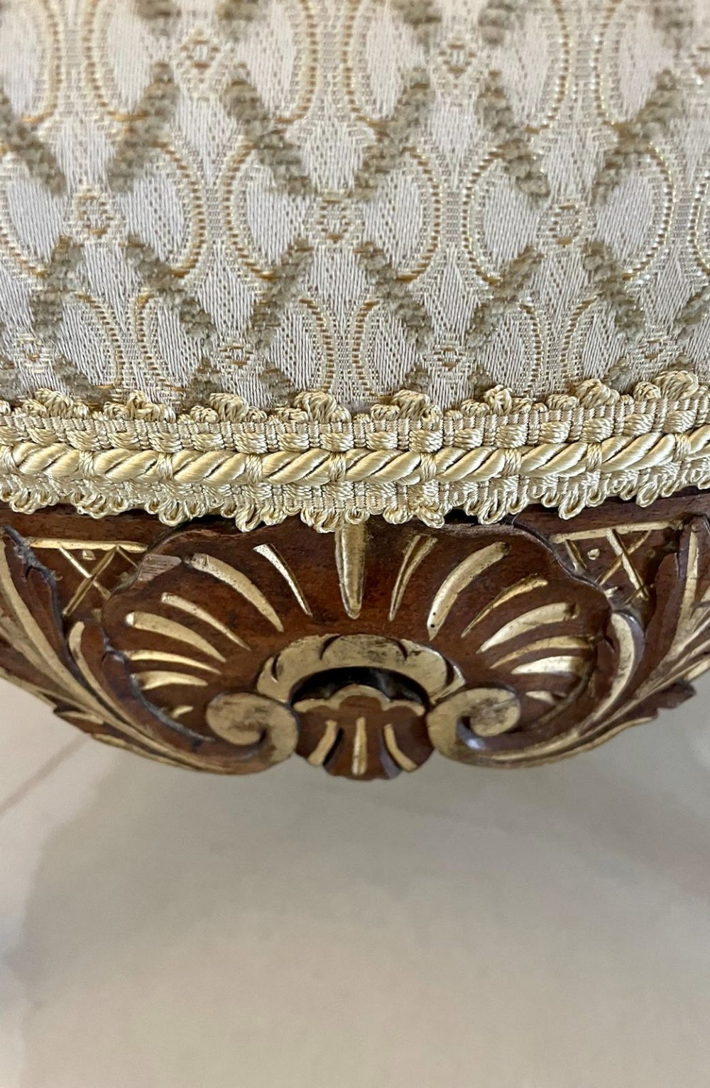 An antique Victorian low stool featuring carved walnut legs with gilt highlights and a beige geometric patterned upholstered top. View II