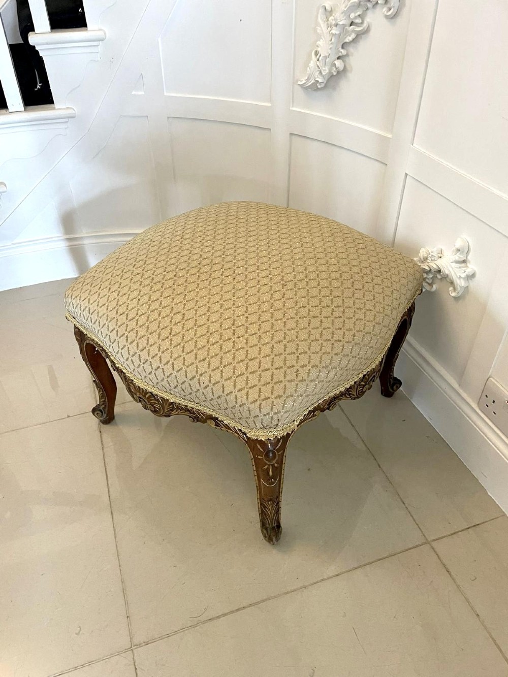 An antique Victorian low stool featuring carved walnut legs with gilt highlights and a beige geometric patterned upholstered top. View IV