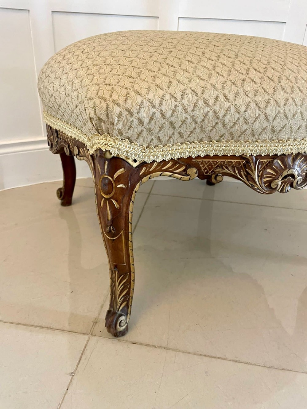An antique Victorian low stool featuring carved walnut legs with gilt highlights and a beige geometric patterned upholstered top. View V