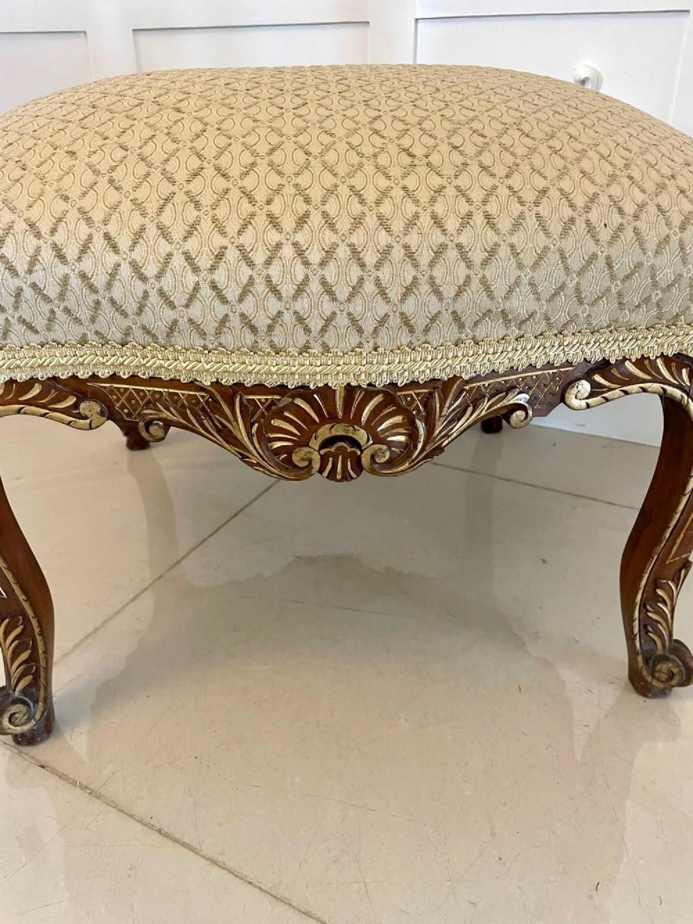 An antique Victorian low stool featuring carved walnut legs with gilt highlights and a beige geometric patterned upholstered top. View VI