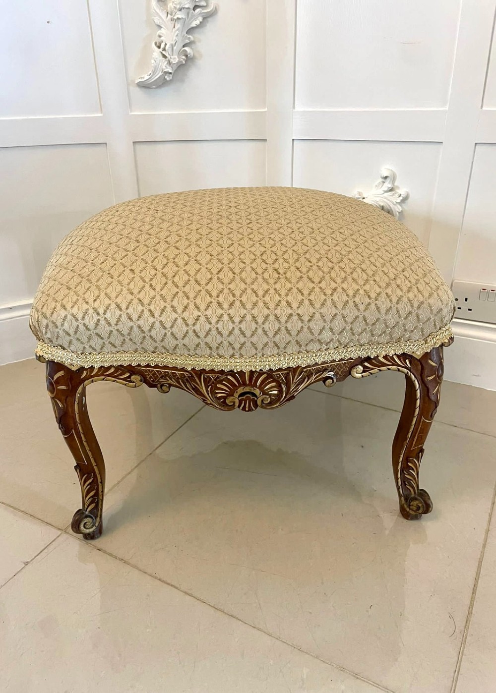 An antique Victorian low stool featuring carved walnut legs with gilt highlights and a beige geometric patterned upholstered top. View VII