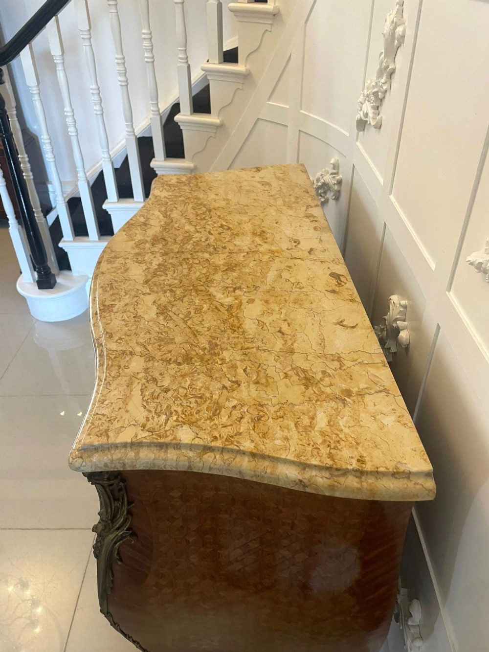 A French Louis XV style serpentine bombe commode featuring a variegated beige marble top, geometric parquetry timber veneer, three drawers, and decorative cast brass mounts. View IV