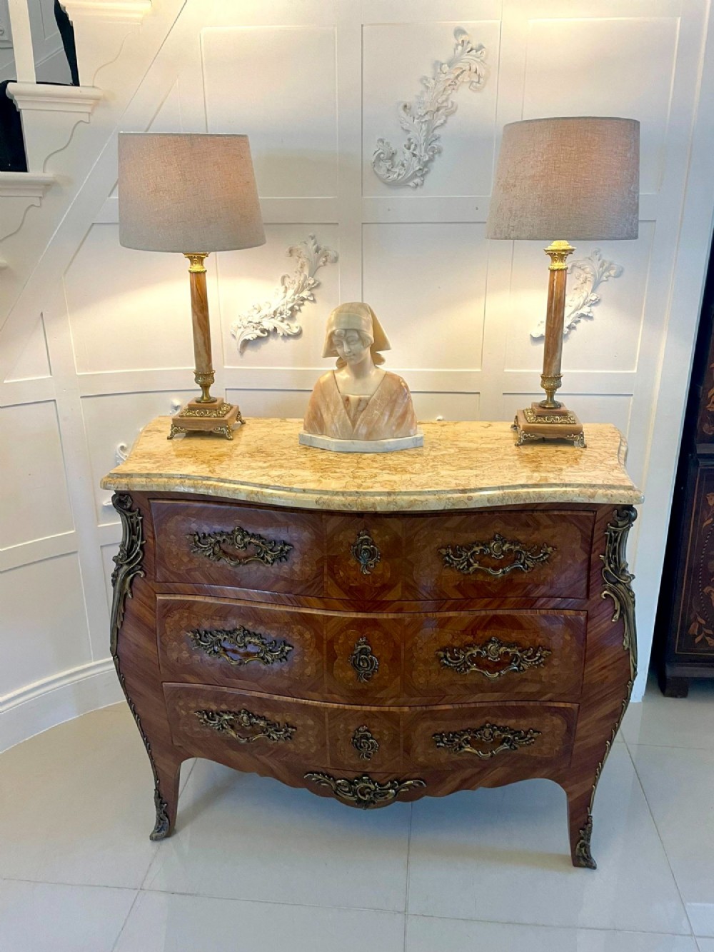 A French Louis XV style serpentine bombe commode featuring a variegated beige marble top, geometric parquetry timber veneer, three drawers, and decorative cast brass mounts. View V