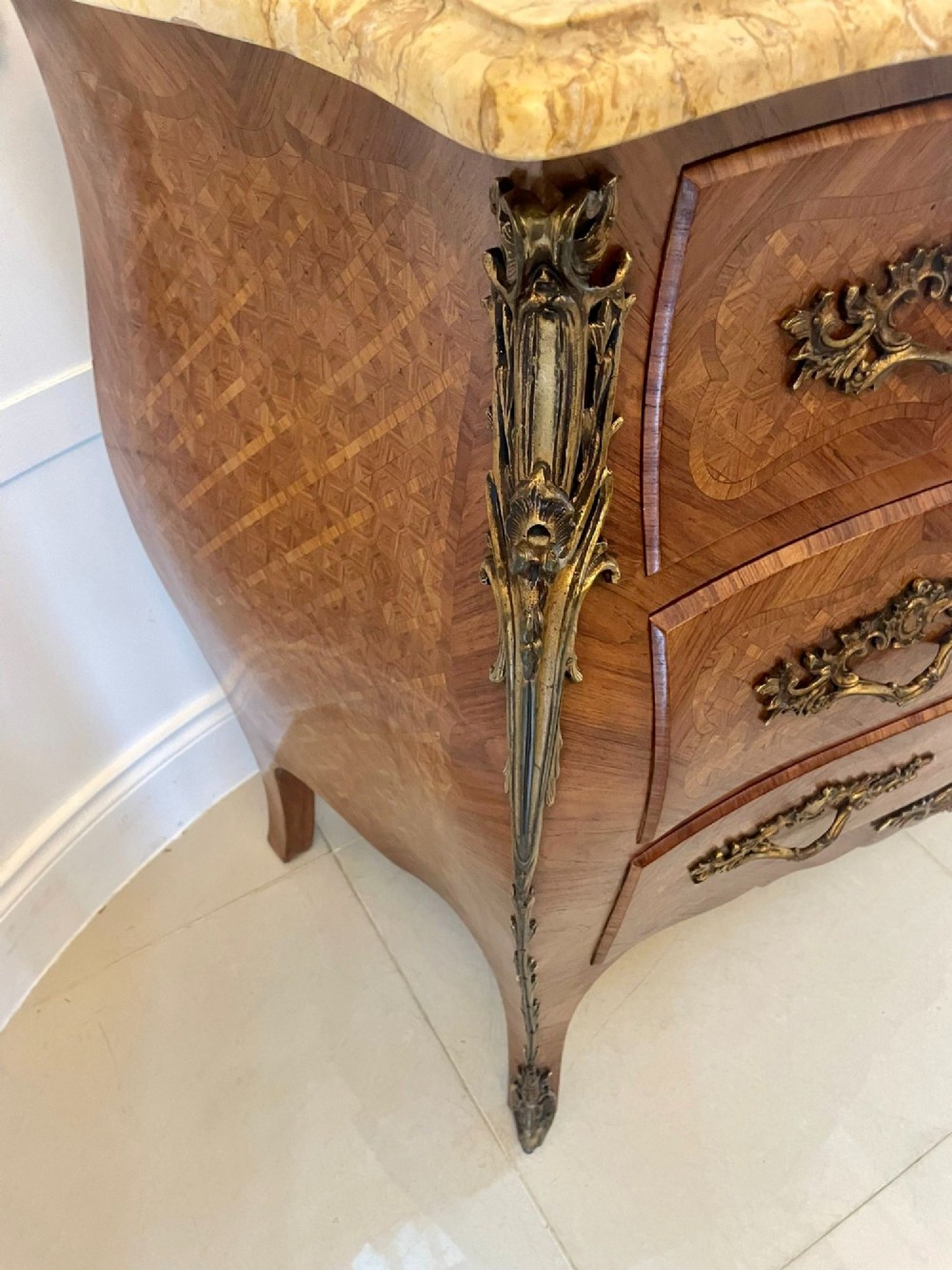 A French Louis XV style serpentine bombe commode featuring a variegated beige marble top, geometric parquetry timber veneer, three drawers, and decorative cast brass mounts. View VIII