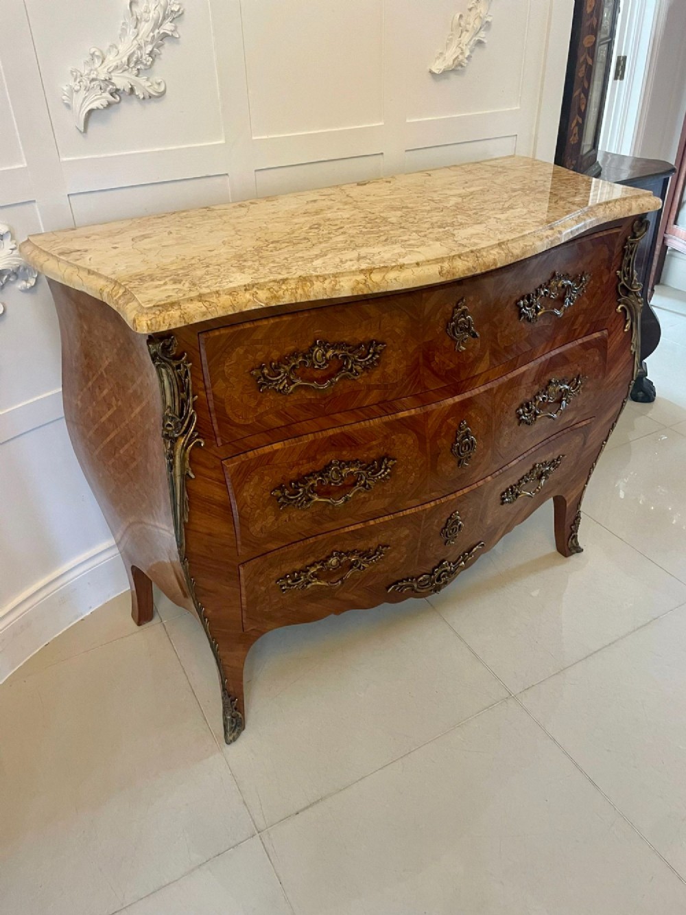 A French Louis XV style serpentine bombe commode featuring a variegated beige marble top, geometric parquetry timber veneer, three drawers, and decorative cast brass mounts. View XII