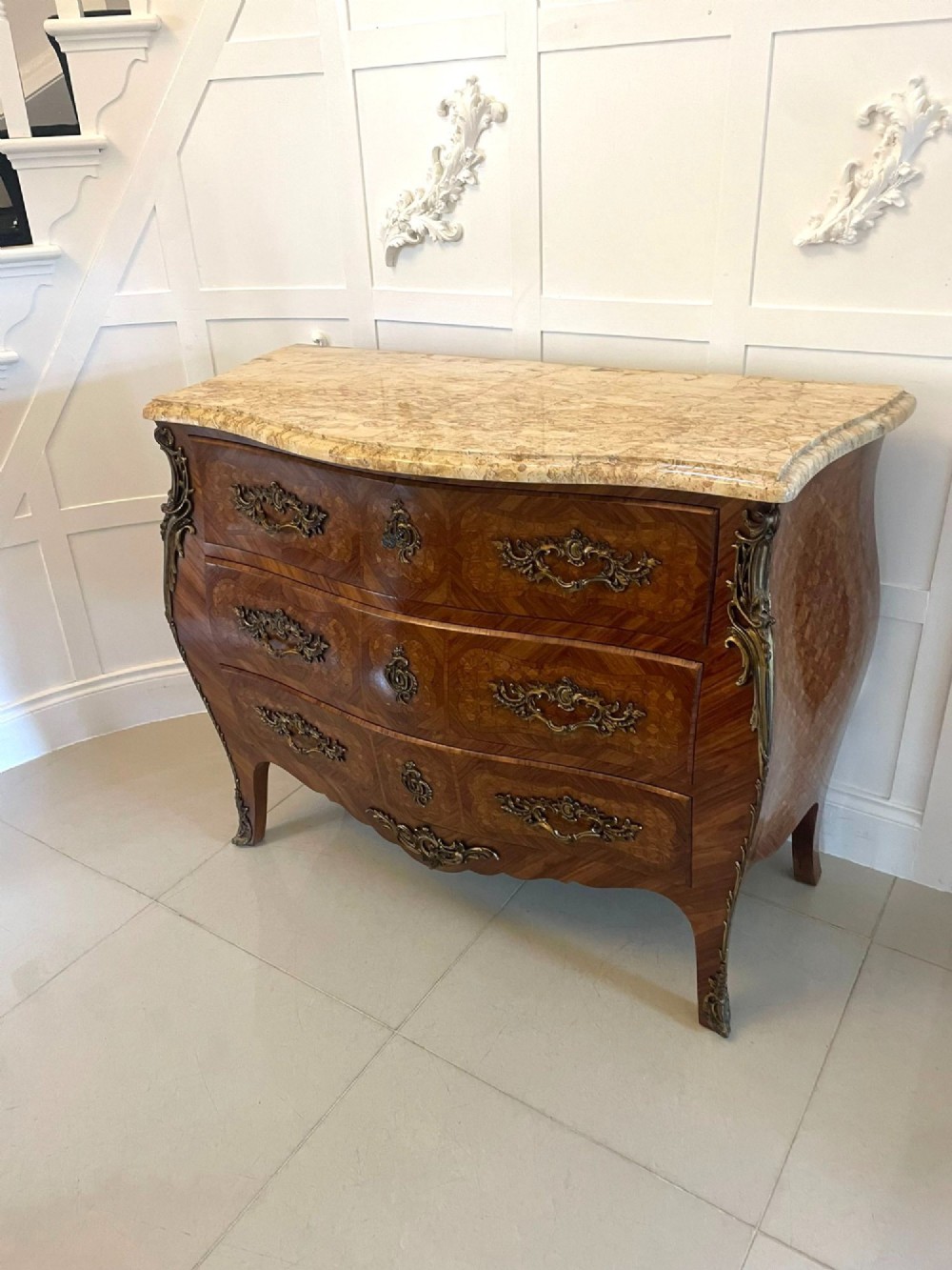 A French Louis XV style serpentine bombe commode featuring a variegated beige marble top, geometric parquetry timber veneer, three drawers, and decorative cast brass mounts. View XIV