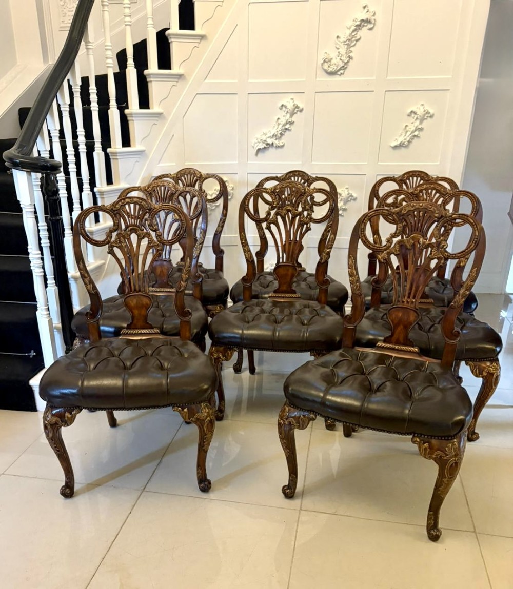 Set of eight Edwardian carved walnut dining chairs featuring pierced backrests, gilded highlights, cabriole legs, and dark brown button-tufted leather seats.