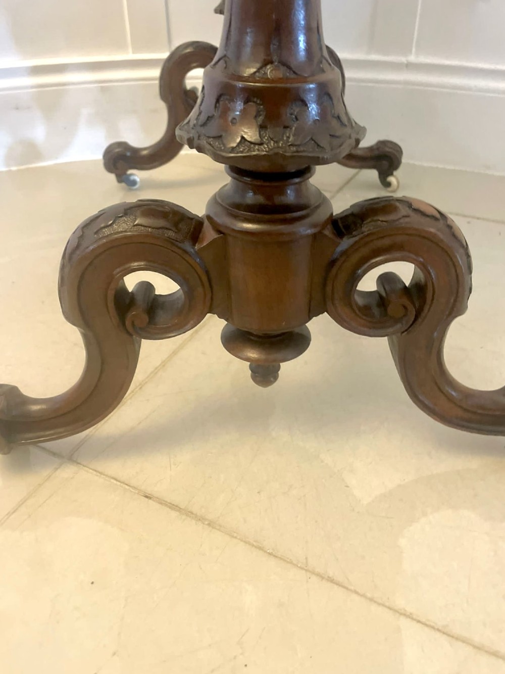 An antique Victorian oval lamp table crafted from burr walnut with turned end supports, a central stretcher, and carved legs with castors. View II