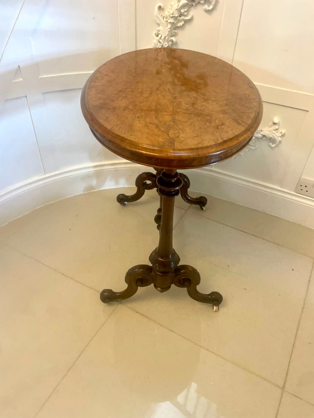 An antique Victorian oval lamp table crafted from burr walnut with turned end supports, a central stretcher, and carved legs with castors. View III