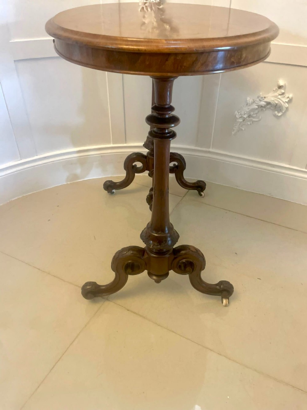An antique Victorian oval lamp table crafted from burr walnut with turned end supports, a central stretcher, and carved legs with castors. View IV