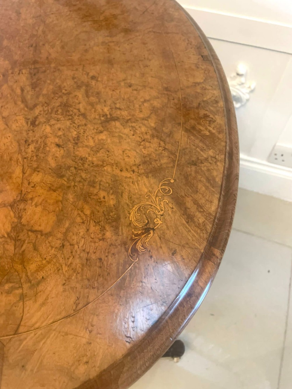 An antique Victorian oval lamp table crafted from burr walnut with turned end supports, a central stretcher, and carved legs with castors. View V