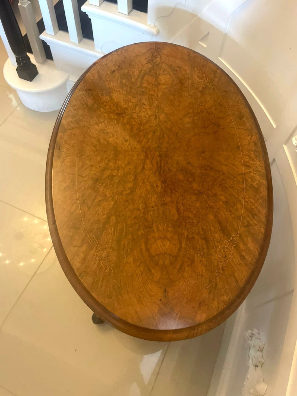An antique Victorian oval lamp table crafted from burr walnut with turned end supports, a central stretcher, and carved legs with castors. View VI