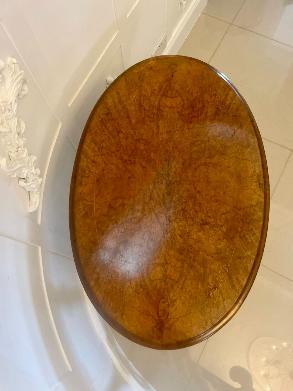 An antique Victorian oval lamp table crafted from burr walnut with turned end supports, a central stretcher, and carved legs with castors. View VII