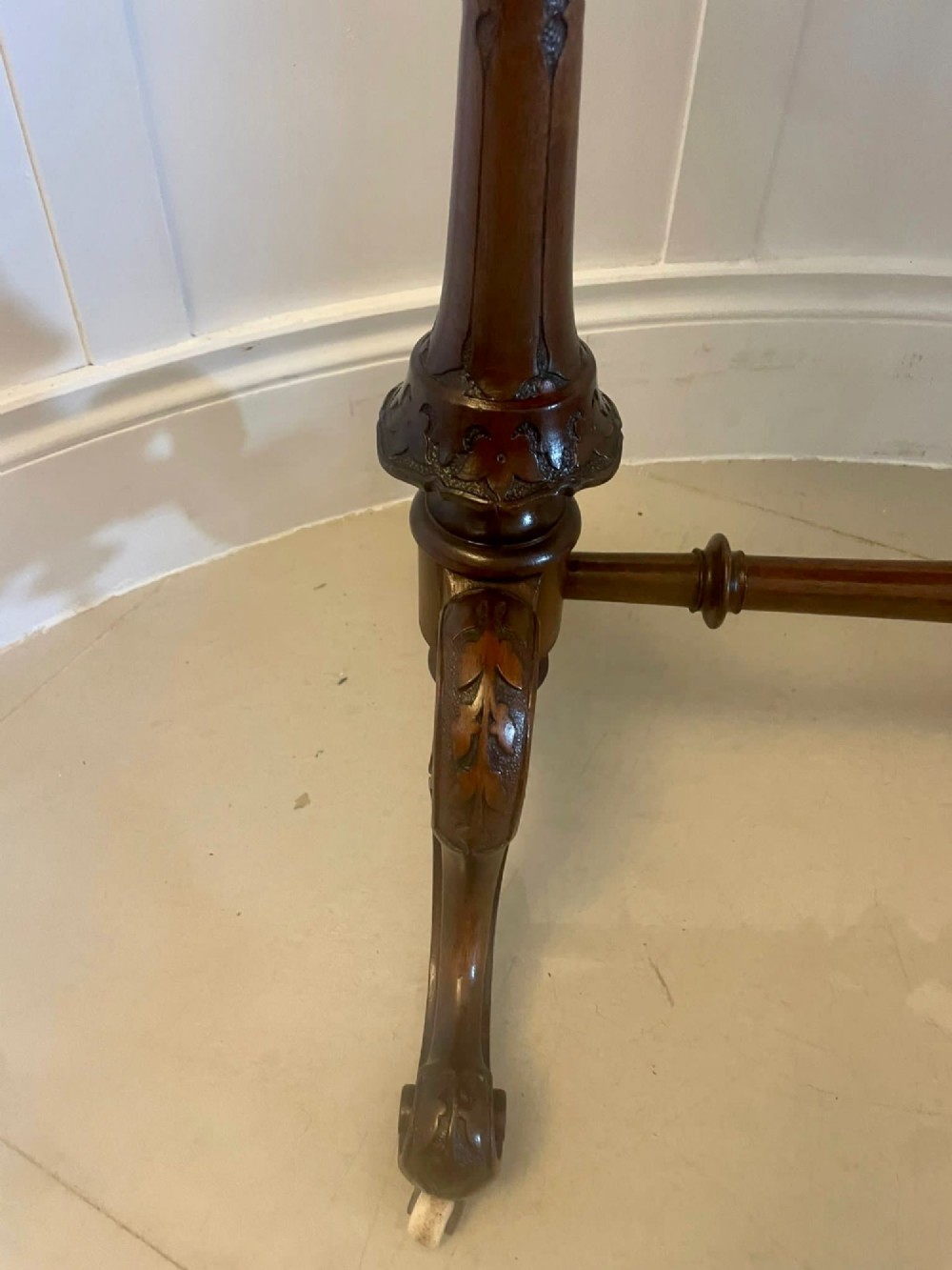 An antique Victorian oval lamp table crafted from burr walnut with turned end supports, a central stretcher, and carved legs with castors. View XII