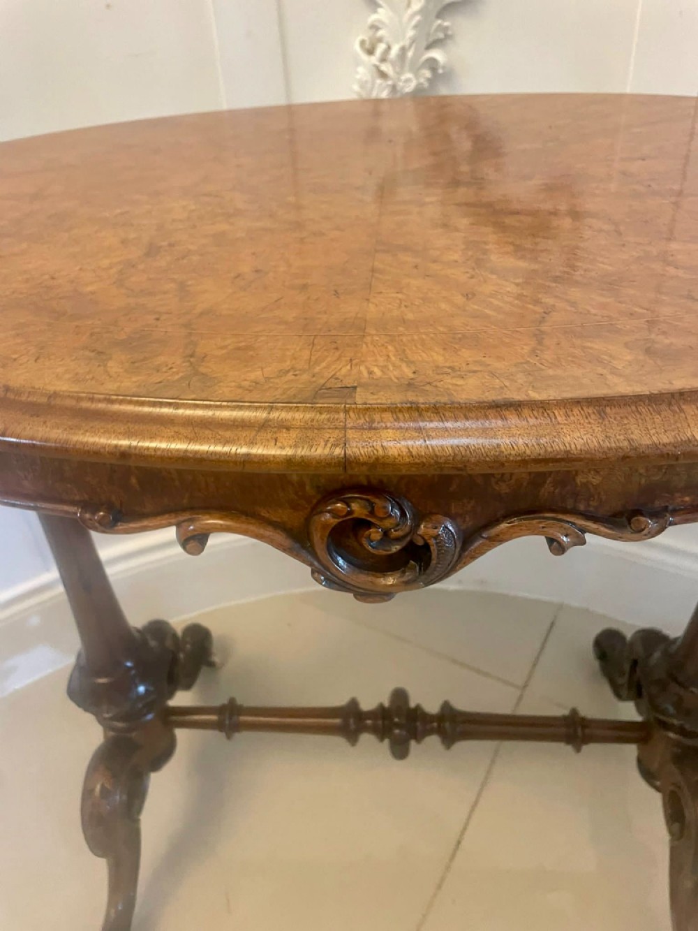 An antique Victorian oval lamp table crafted from burr walnut with turned end supports, a central stretcher, and carved legs with castors. View XIII