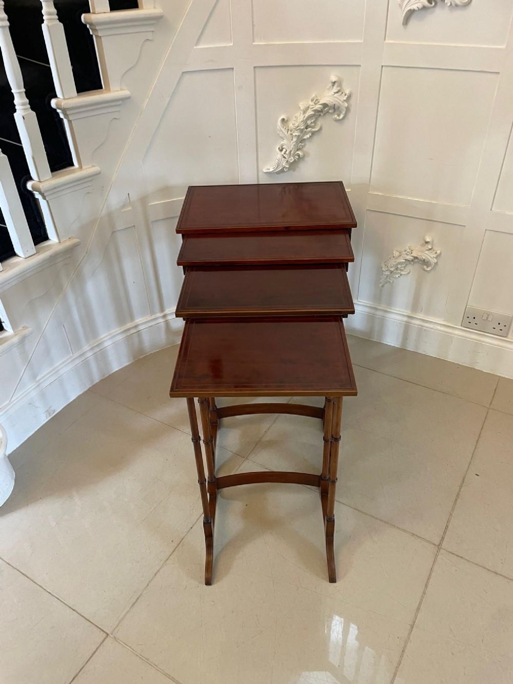 A set of four graduated Edwardian mahogany nesting tables with inlaid tops and slender turned legs arranged in a stepped display.