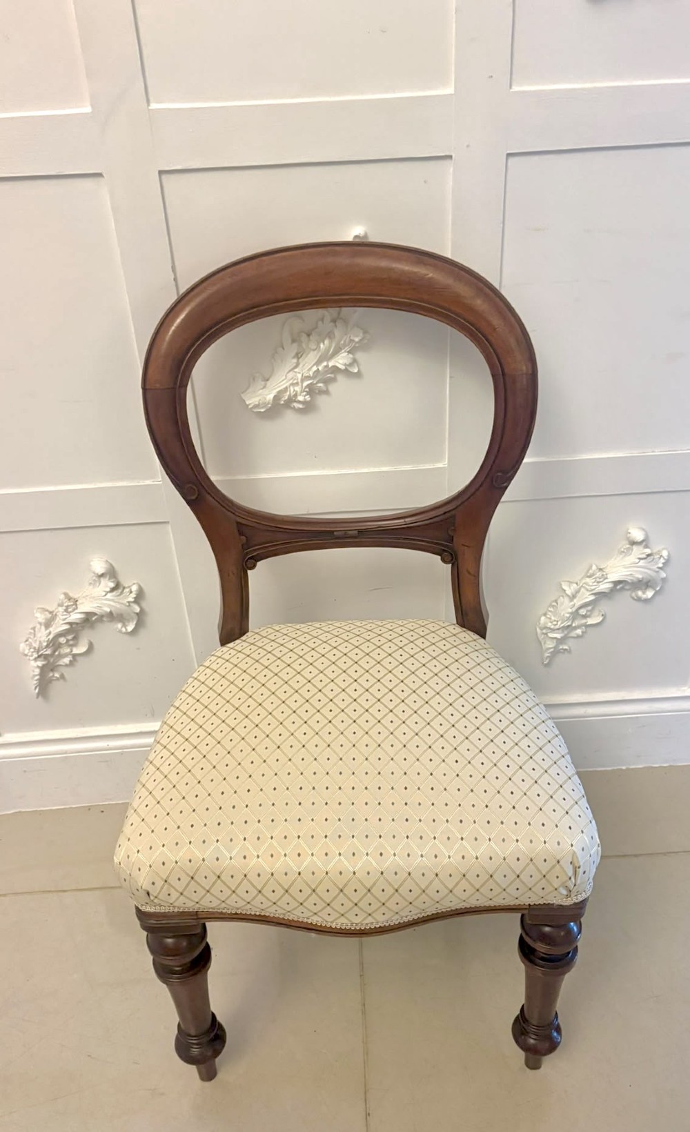 A set of four antique Victorian mahogany dining chairs featuring open balloon-shaped backrests, turned front legs, and cream patterned upholstery. View X