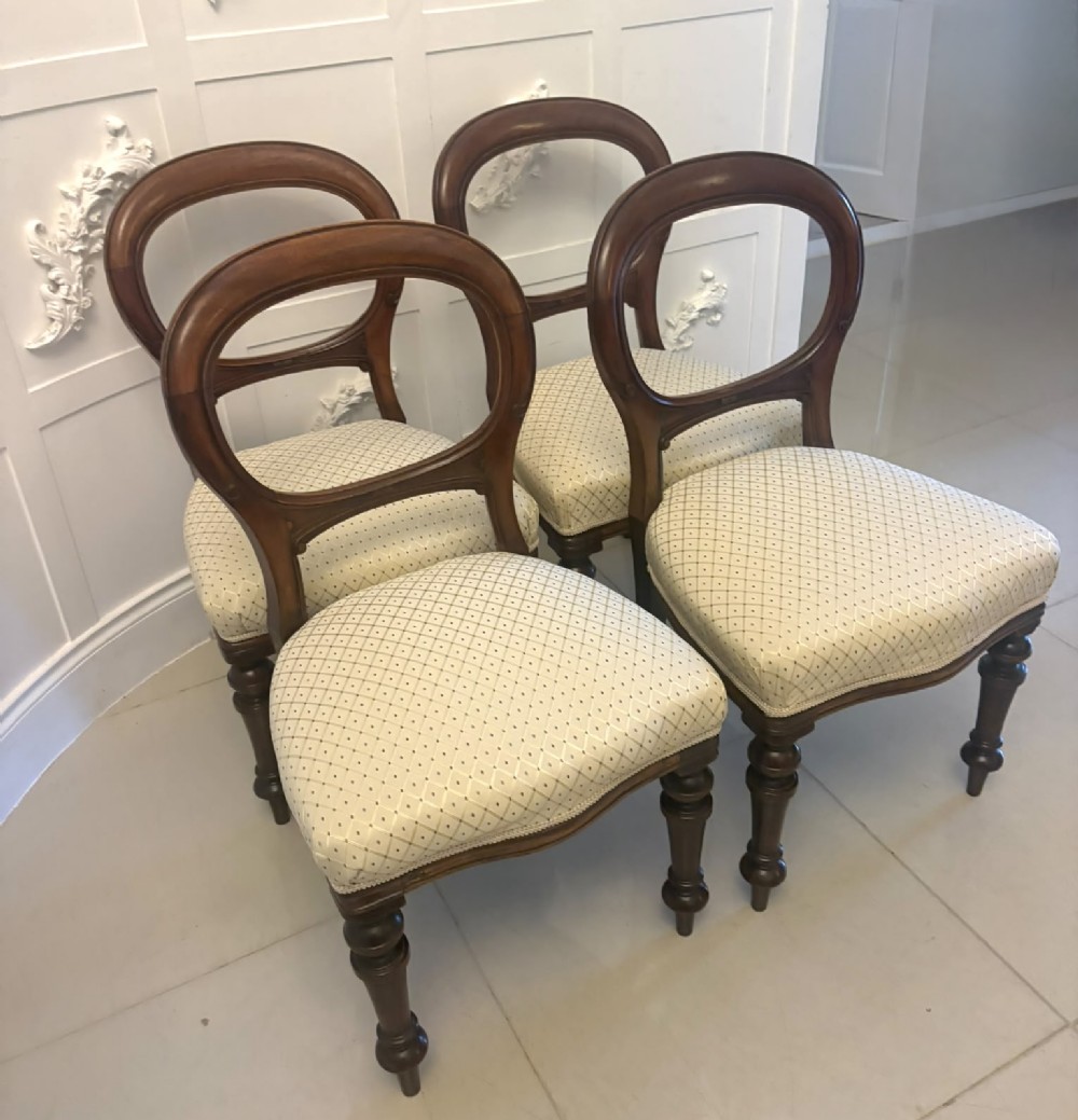 A set of four antique Victorian mahogany dining chairs featuring open balloon-shaped backrests, turned front legs, and cream patterned upholstery.