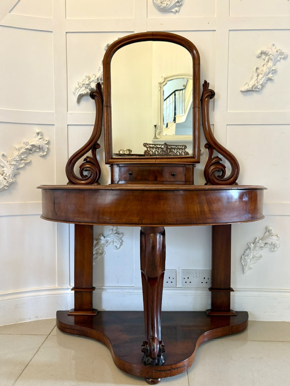 An antique Victorian mahogany dressing table featuring an arched swing mirror with scroll supports above a curved tabletop and shaped platform base.