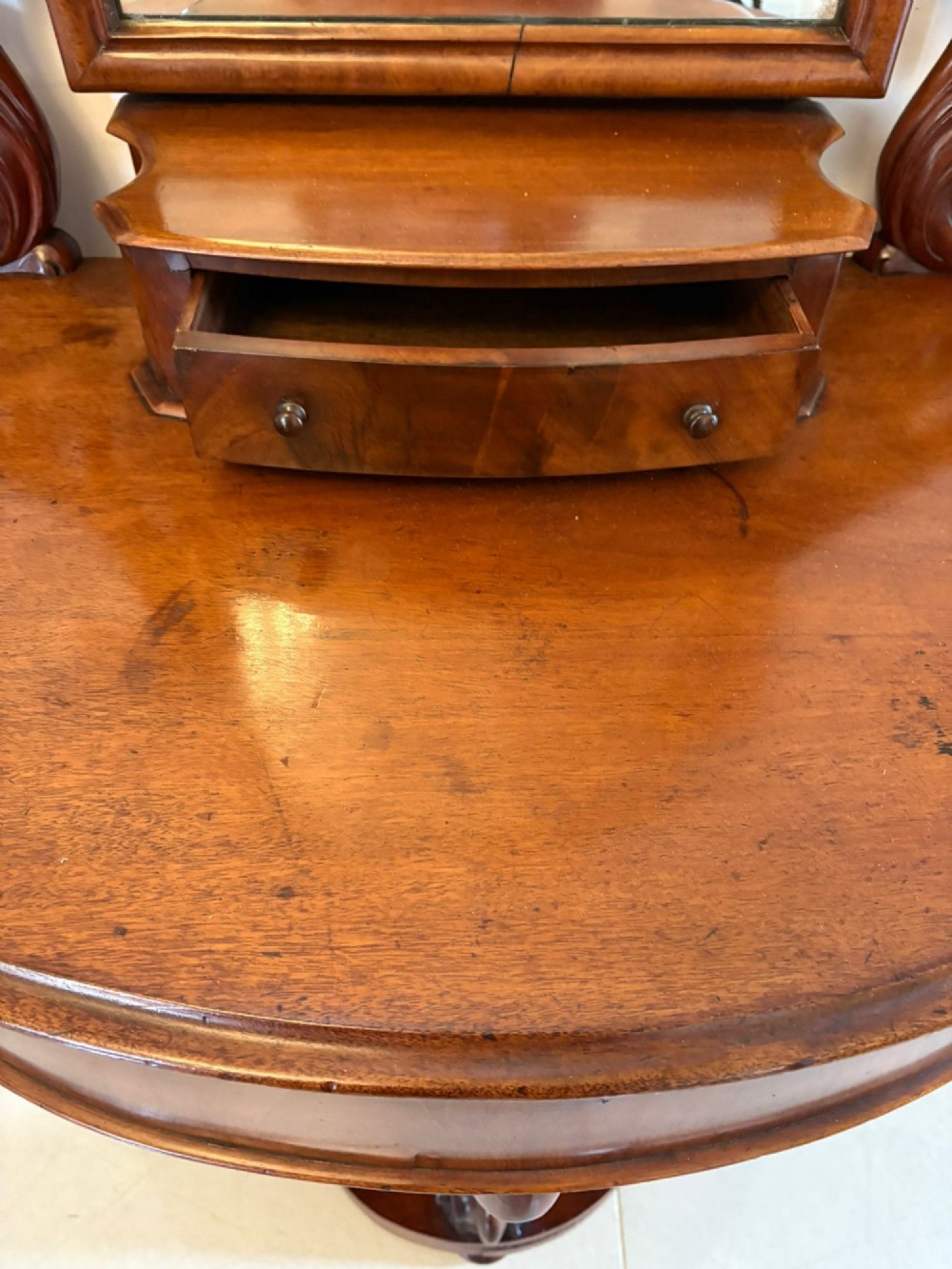 An antique Victorian mahogany dressing table featuring an arched swing mirror with scroll supports above a curved tabletop and shaped platform base. View X