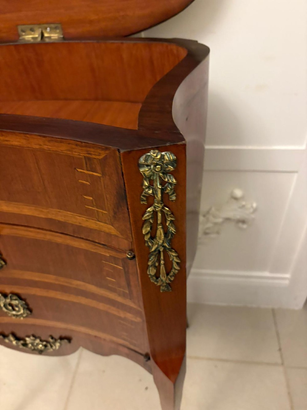 An antique French Louis XV style wooden side cabinet featuring three marquetry drawers, brass rim, decorative corner mounts, and slender cabriole legs. View III