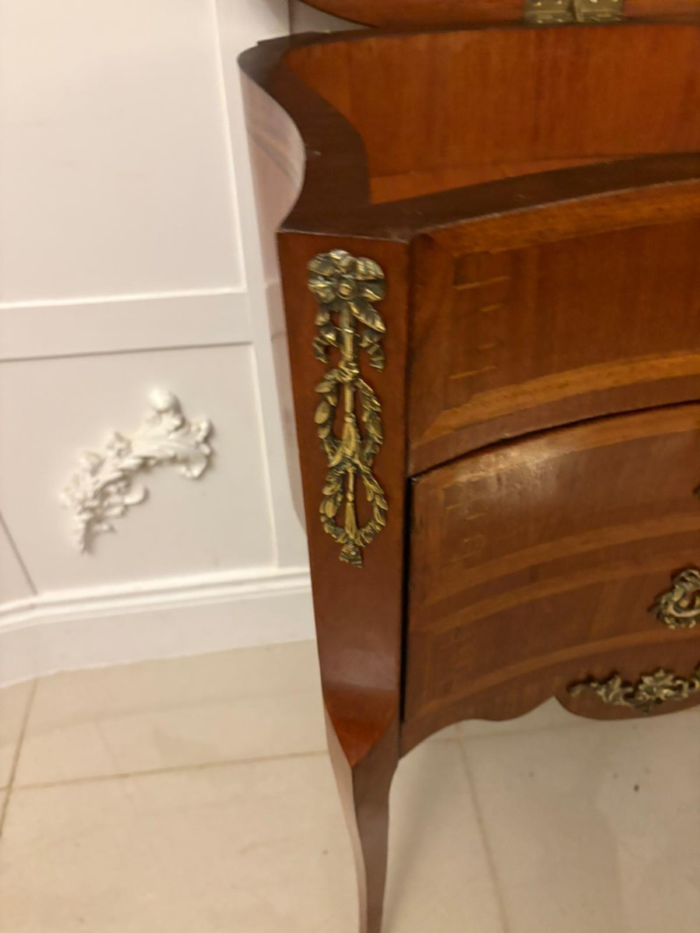 An antique French Louis XV style wooden side cabinet featuring three marquetry drawers, brass rim, decorative corner mounts, and slender cabriole legs. View VI