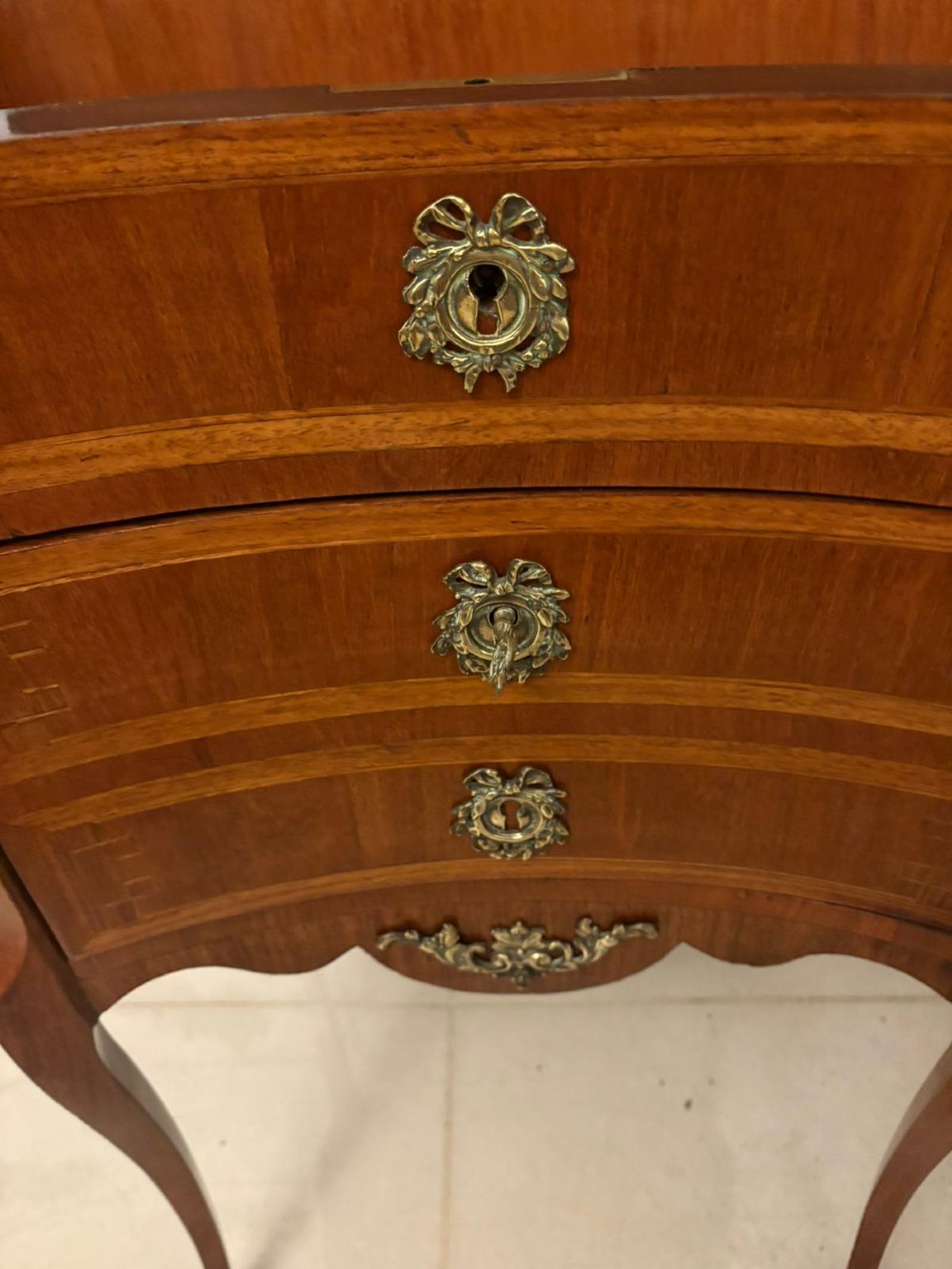 An antique French Louis XV style wooden side cabinet featuring three marquetry drawers, brass rim, decorative corner mounts, and slender cabriole legs. View X