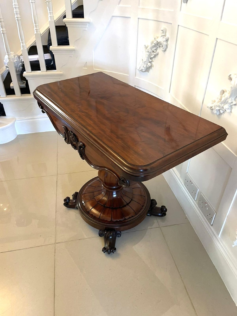 A Victorian mahogany fold-over card table featuring a rectangular top, carved apron, turned central pedestal, and four scroll feet. View XII