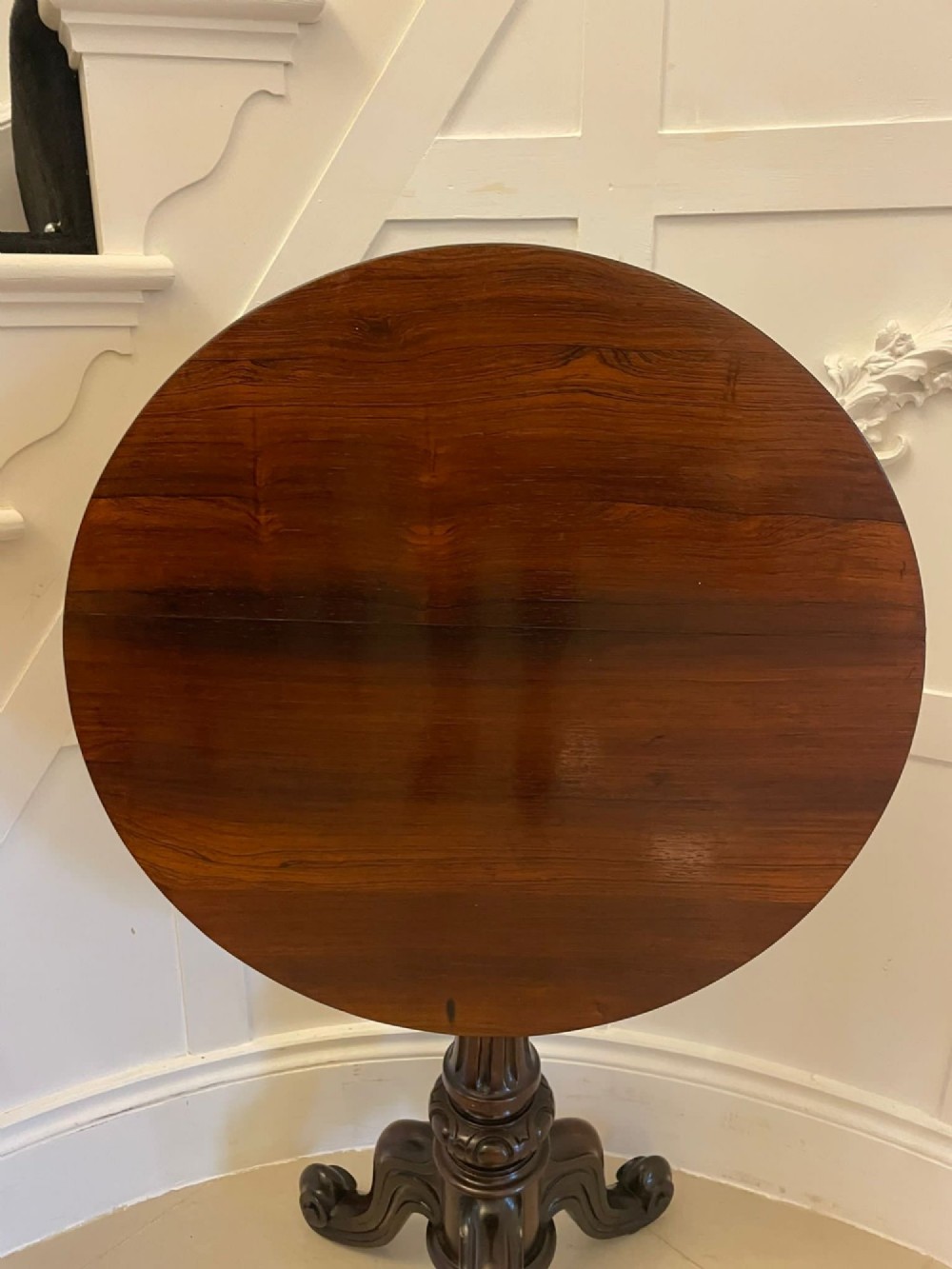 A Victorian rosewood circular lamp table shown in a tilted position, featuring a turned central column and carved tripod legs with scroll feet. View X