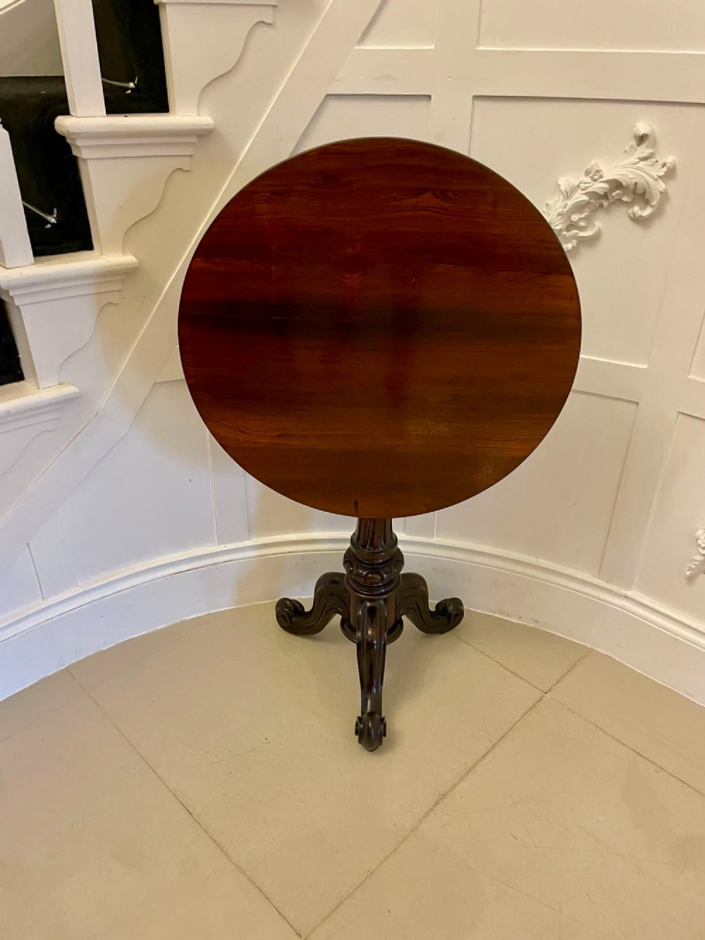 A Victorian rosewood circular lamp table shown in a tilted position, featuring a turned central column and carved tripod legs with scroll feet.
