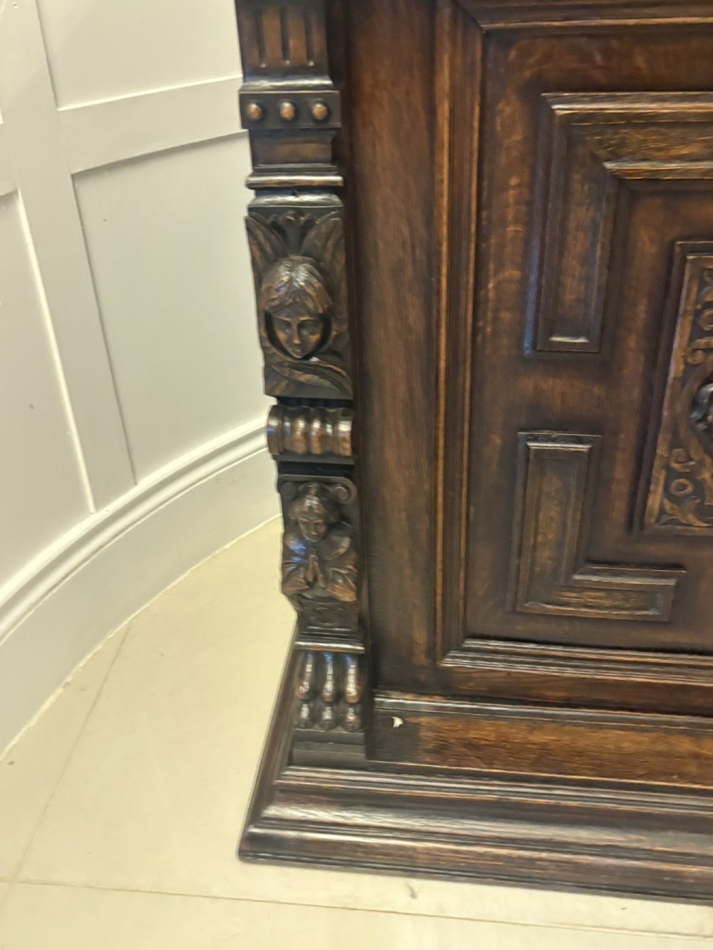 A dark carved oak sideboard featuring geometric panelled cupboard doors with central lion mask carvings and a detailed relief frieze. View V