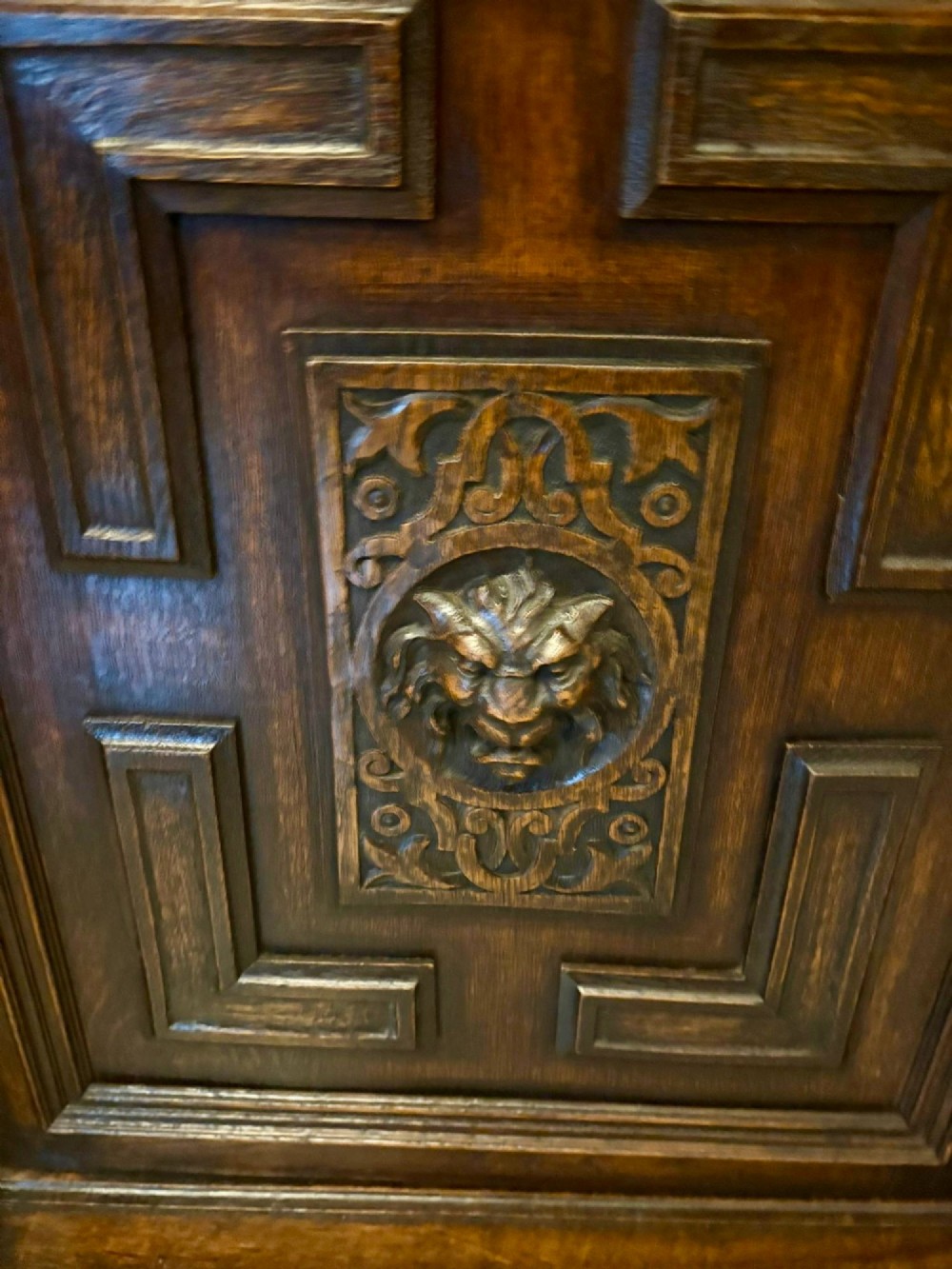A dark carved oak sideboard featuring geometric panelled cupboard doors with central lion mask carvings and a detailed relief frieze. View VIII