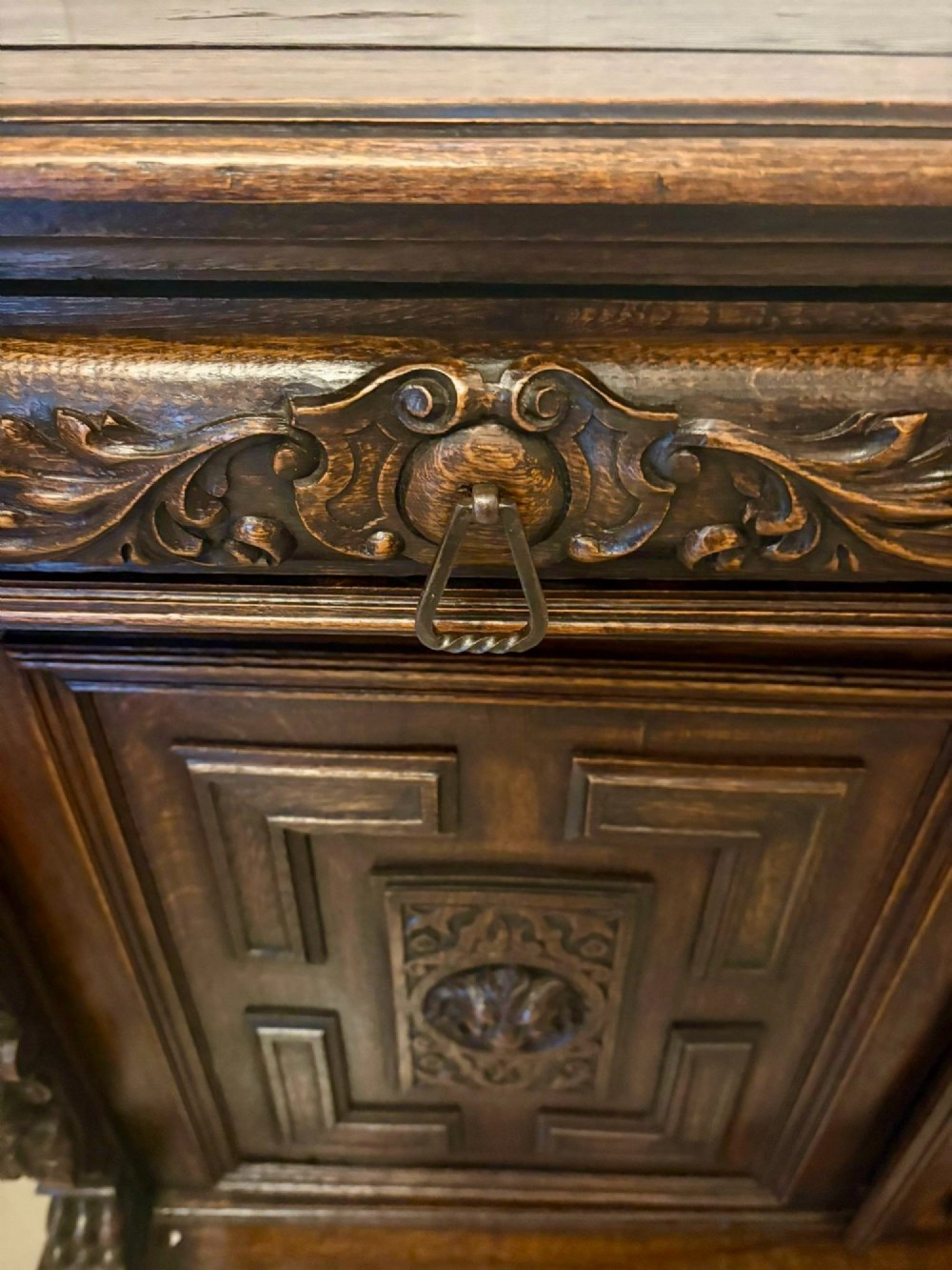A dark carved oak sideboard featuring geometric panelled cupboard doors with central lion mask carvings and a detailed relief frieze. View X