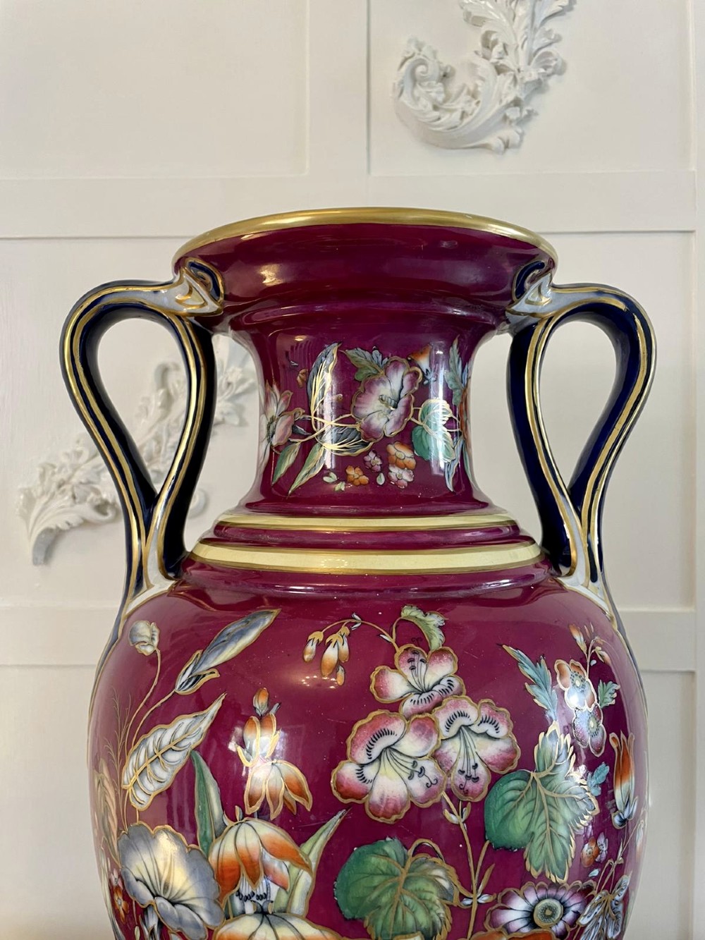 A large Victorian twin-handled porcelain urn vase in vibrant magenta featuring hand-painted botanical florals, navy blue handles, and gold leaf gilding. View VI