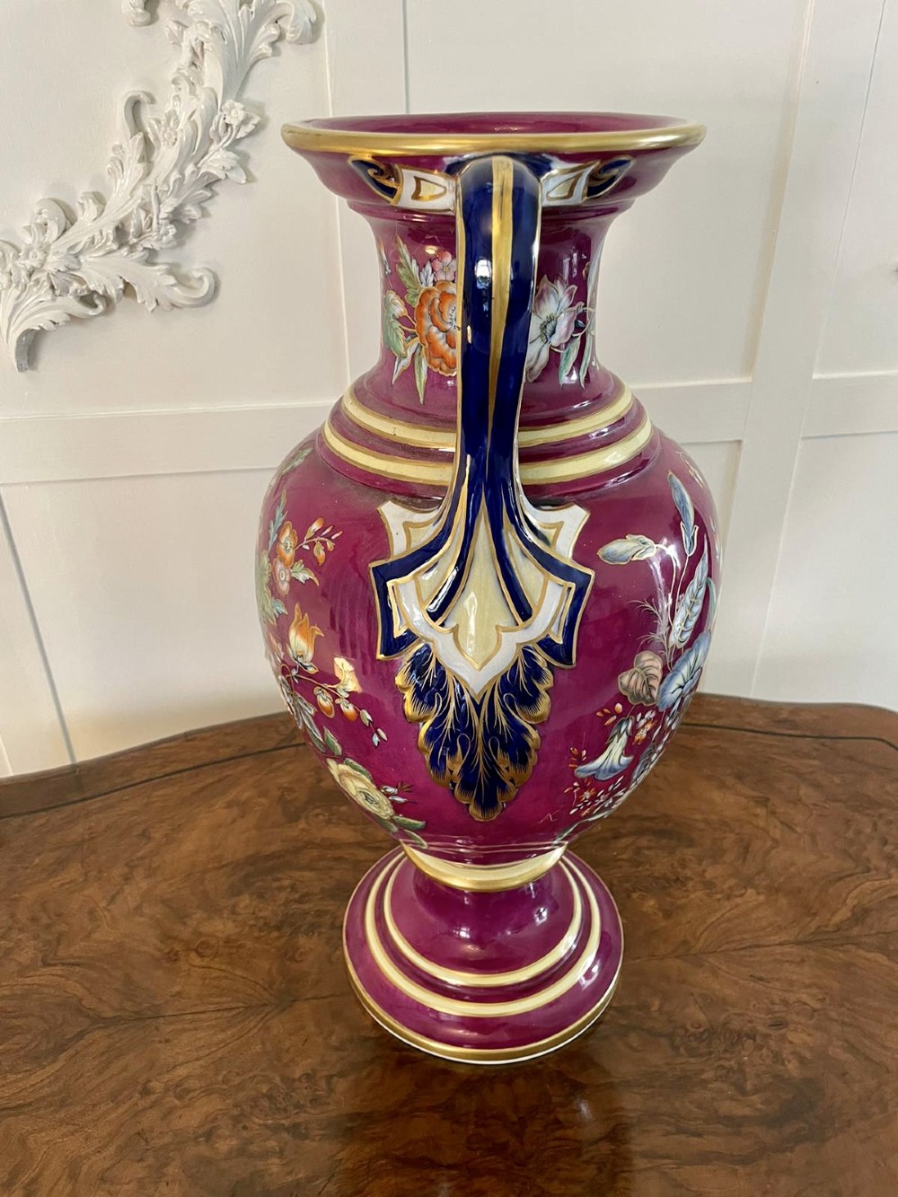 A large Victorian twin-handled porcelain urn vase in vibrant magenta featuring hand-painted botanical florals, navy blue handles, and gold leaf gilding. View VIII