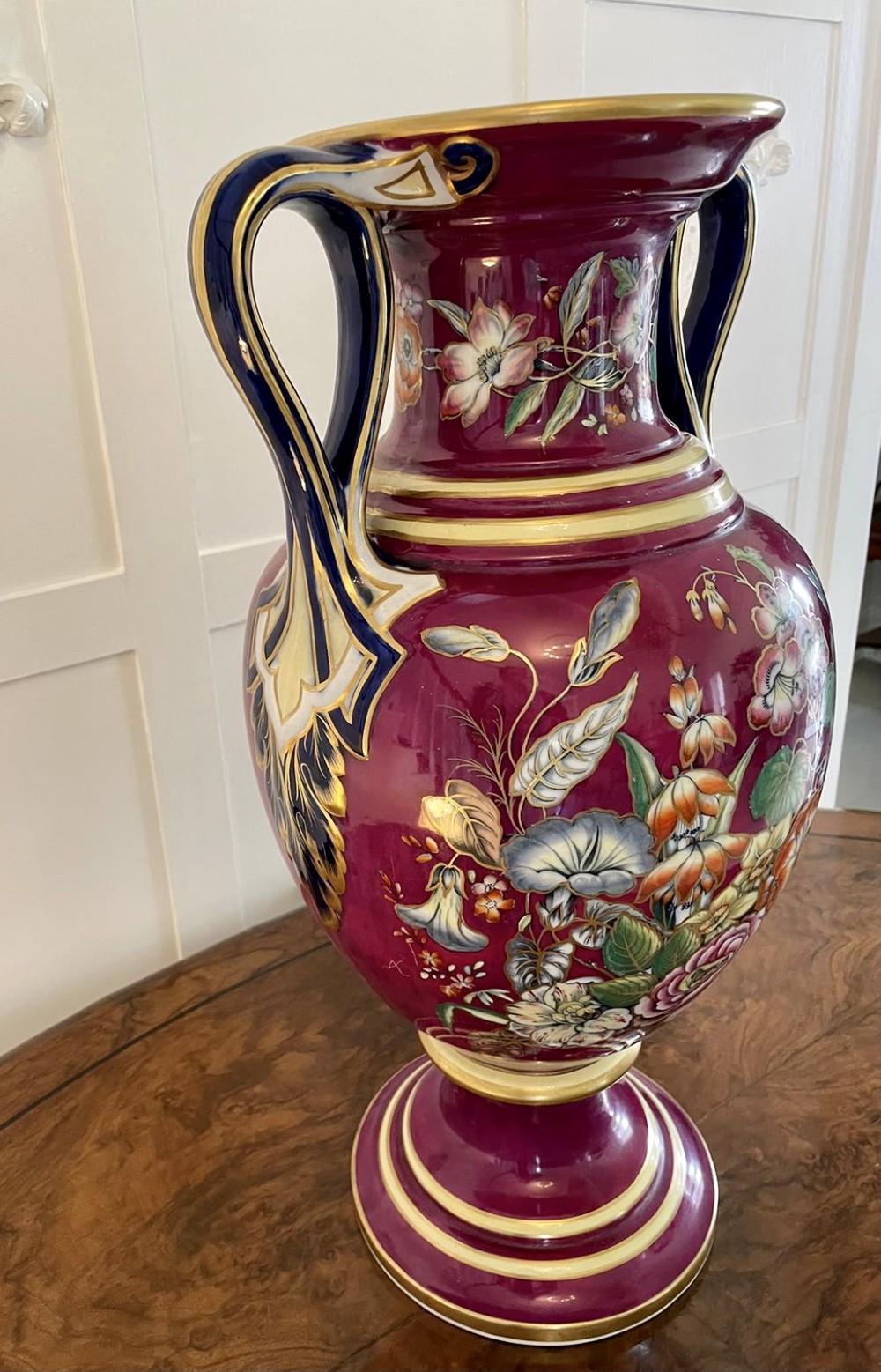 A large Victorian twin-handled porcelain urn vase in vibrant magenta featuring hand-painted botanical florals, navy blue handles, and gold leaf gilding. View IX