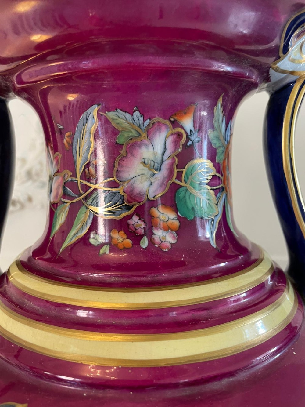 A large Victorian twin-handled porcelain urn vase in vibrant magenta featuring hand-painted botanical florals, navy blue handles, and gold leaf gilding. View X